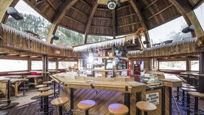 Een rustiek houten interieur met een bar in het midden, houten krukken en grote ramen met uitzicht op de omgeving.