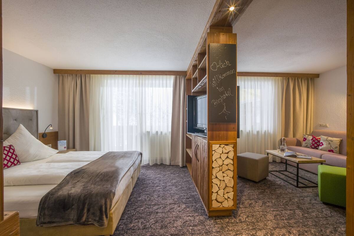 Une chambre d’hôtel avec un lit, un canapé, une télévision et une armoire en bois.