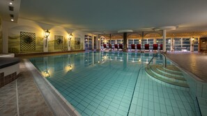 En inomhuspool med kaklade väggar, röda solstolar och väggmonterade lampor.