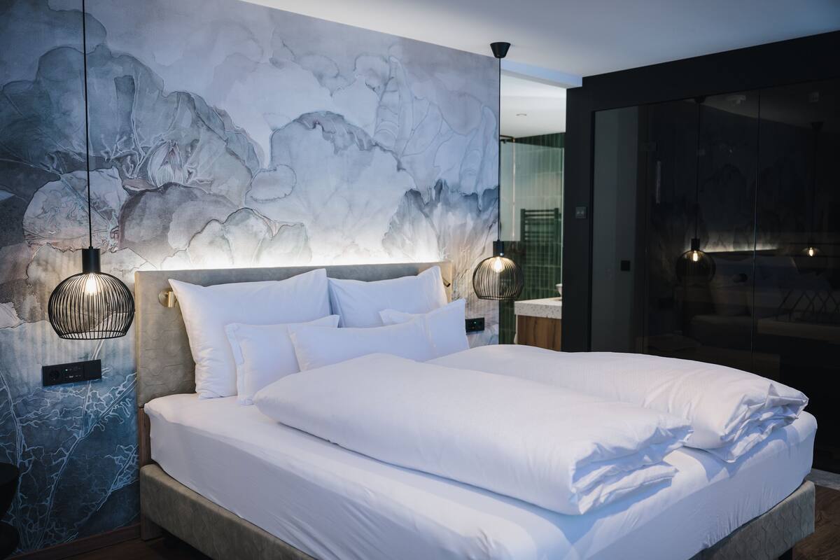 Une chambre moderne avec un grand lit, une fresque murale en marbre et deux lampes suspendues.