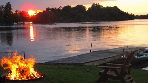 A lakeside scene with a fire pit and a dock with boats. - Cozy Waterfront on Puslinch Lake (Puslinch)