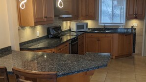 A kitchen with granite countertops, wooden cabinets, a built-in microwave, and a large island with bar stools. - Cozy Waterfront on Puslinch Lake (Puslinch)