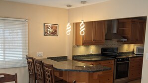 A kitchen with wooden cabinets, a granite countertop, and a dining area with a wooden table and chairs. - Cozy Waterfront on Puslinch Lake (Puslinch)