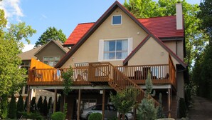 A two-story house with a red roof, a balcony with wooden railings, and a garage with two cars parked inside. - Cozy Waterfront on Puslinch Lake (Puslinch)