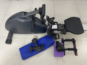 A stationary exercise bike, a blue exercise mat, and a purple foam roller on a tiled floor.