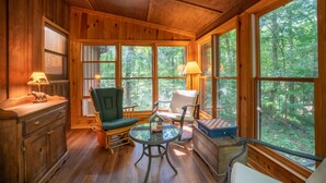 A cozy cabin interior with wooden walls, large windows, a fireplace, and a chessboard.