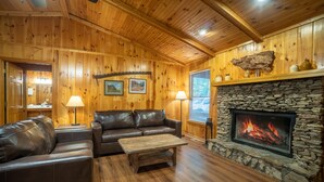 A cozy cabin interior with wooden walls, a stone fireplace, leather sofas, and a wooden coffee table.