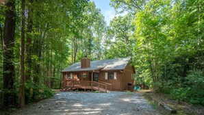 A rustic cabin with a gravel driveway, surrounded by dense forest.