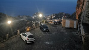 Ein Parkplatz mit einem weißen Auto und einem schwarzen Auto auf einer Kopfsteinpflasterstraße, mit Blick auf eine Küstenstadt mit Gebäuden und einer Klippe.