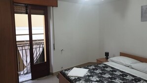 Ein Schlafzimmer mit einem Bett, einem Nachttisch, einer Wandlampe und einer Tür, die auf einen Balkon führt.