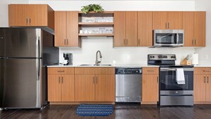 A modern kitchen with wooden cabinets, stainless steel appliances, a coffee shelf, and a dishwasher. - *NEW* Spacious Condo Near Downtown TC (Traverse City)