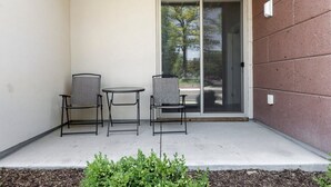 A covered patio with two chairs and a small table, a sliding glass door, and a concrete floor. - *NEW* Spacious Condo Near Downtown TC (Traverse City)