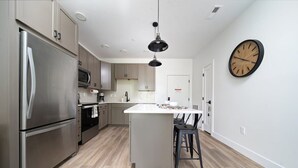 A modern kitchen with stainless steel appliances, a central island, and a wall-mounted clock. - 1BR I King + Sofa I Walk Shops + DT TC (Traverse City)