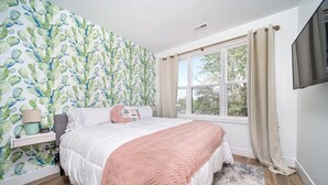 A bedroom with a bed, a nightstand, a window with curtains, and a wall with a cactus pattern. - 1BR I King + Sofa I Walk Shops + DT TC (Traverse City)