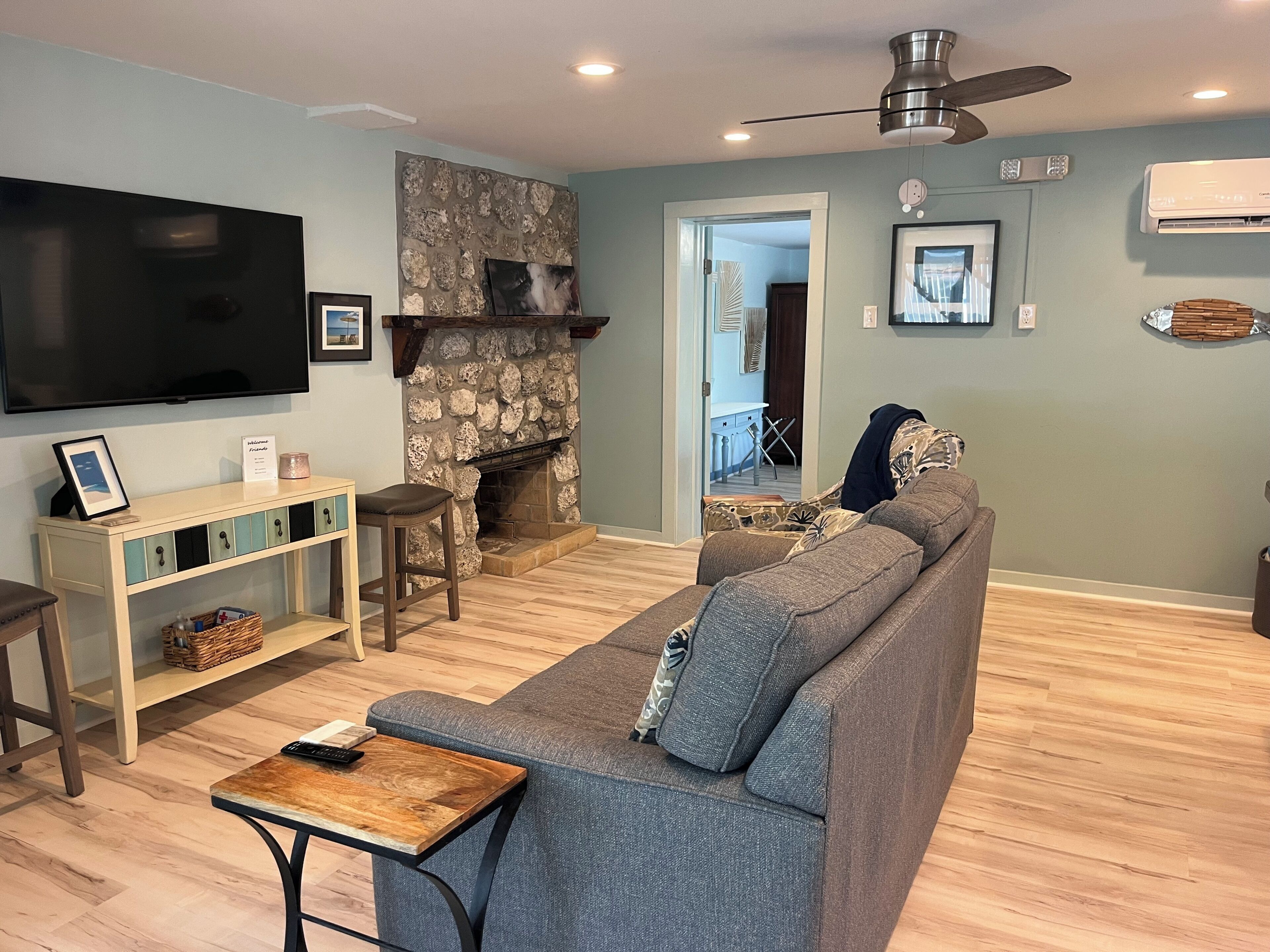 A living room with a stone fireplace, a flat-screen TV, a sofa, and a ceiling fan.