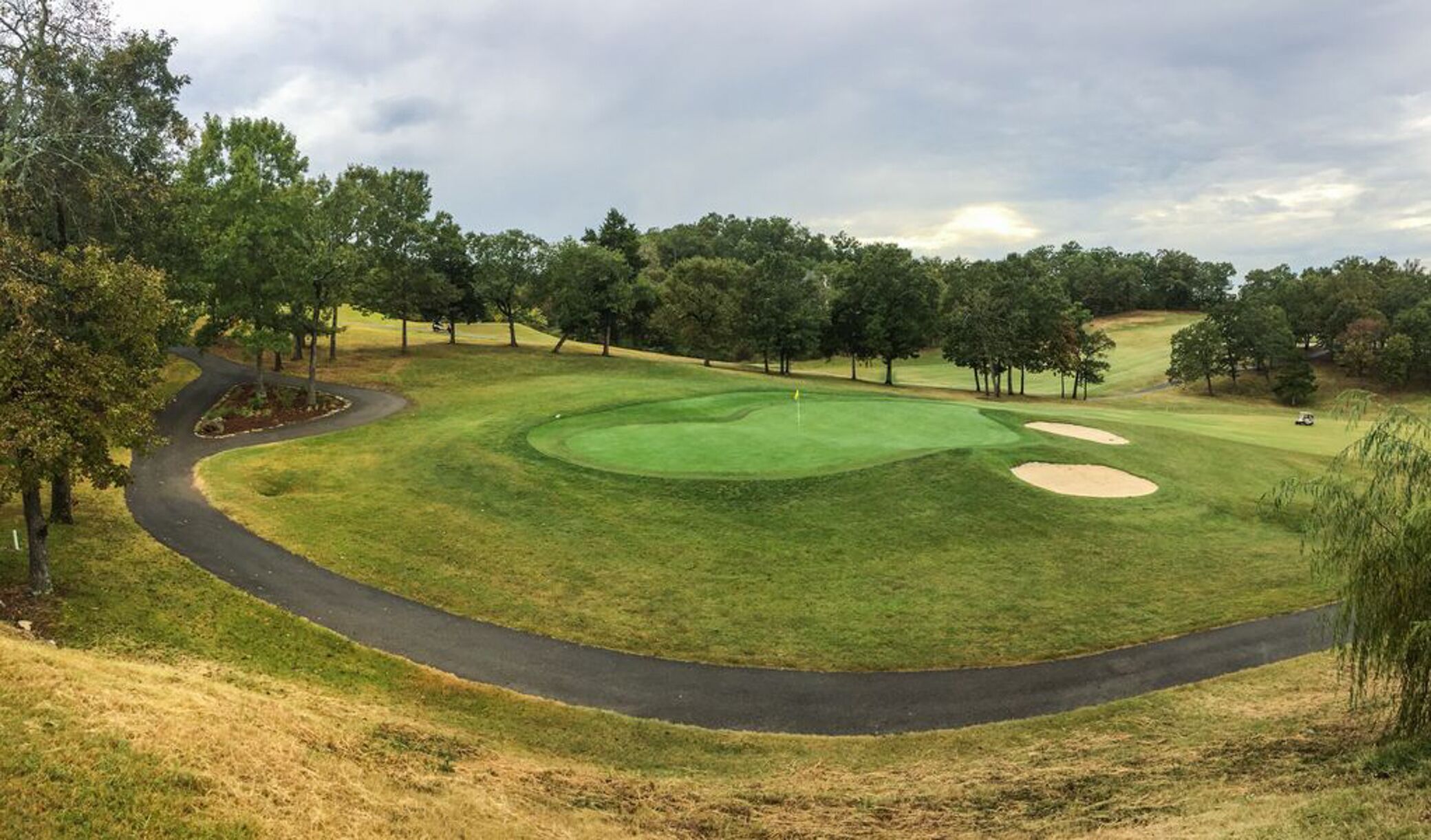 Un parcours de golf avec un chemin sinueux, des bunkers de sable et un drapeau sur le green.