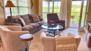 A living room with a sofa, armchairs, a coffee table, and a view through a glass door to a balcony. - Gorgeous Golf Views, Quiet/Large, Resort and Pools (Reeds Spring)