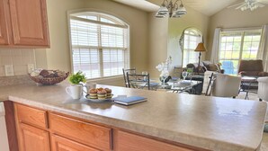 A kitchen with wooden cabinets, a marble countertop, and a dining area with a table set for two. - Gorgeous Golf Views, Quiet/Large, Resort and Pools (Reeds Spring)