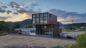 A modern two-story building with large windows and a balcony, surrounded by a landscaped area with outdoor seating.