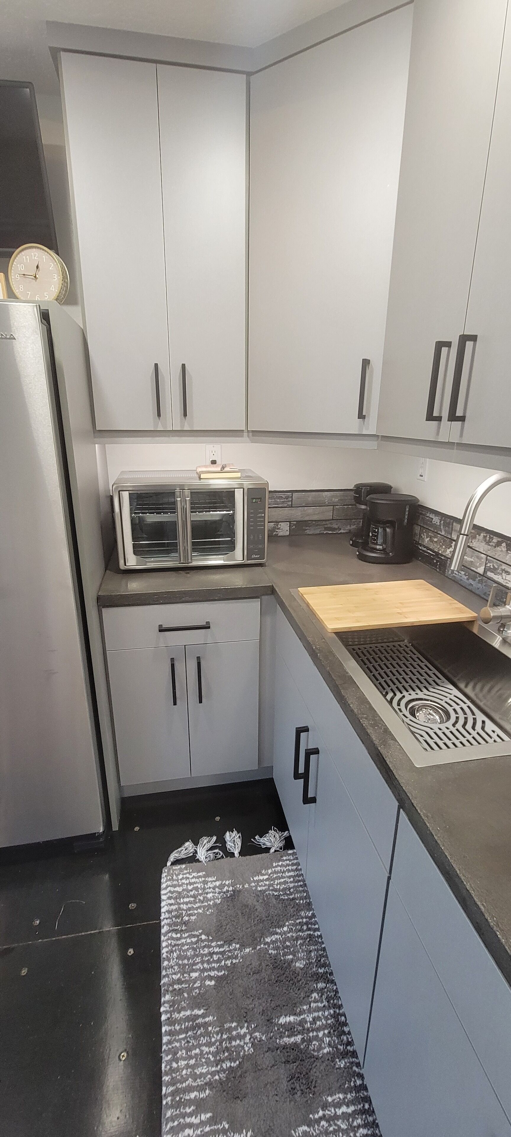 Una cocina compacta con armarios blancos, un refrigerador de acero inoxidable, un microondas y una cafetera.