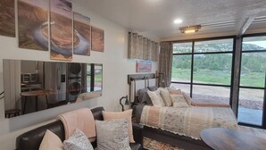A modern room with a bed, a sofa, a dining table, and a large window offering a view of the outdoors.