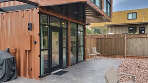 A modern building with a covered patio, sliding glass doors, and a wooden fence.