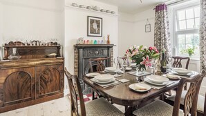 A dining room with a wooden table set for six, a fireplace, and a window with curtains. - 4 bedroom accommodation in Bacton, Norwich (Bacton, Norwich)