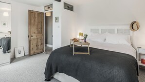 A bedroom with a large bed, a bedside table with glasses and pastries, a wooden door, and a mirror. - 4 bedroom accommodation in Bacton, Norwich (Bacton, Norwich)