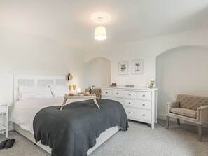 Un dormitorio con cama, mesita de noche, cómoda, silla y una lámpara en el techo.