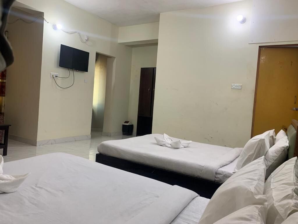 Quarto de hotel com duas camas, uma televisão fixada na parede e uma porta de madeira.