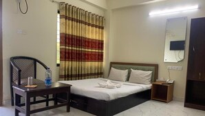 Habitación de hotel con cama, una silla, una mesita, una mesita de noche y un espejo.