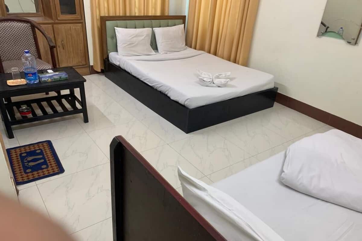 Une chambre d’hôtel avec un lit, une petite table sur laquelle se trouve une bouteille d’eau, une chaise et un tapis bleu sur le sol.