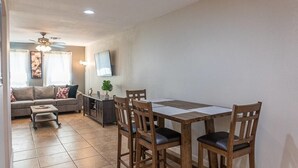 A living room with a sofa, a coffee table, and a dining table with chairs. There is a ceiling fan, a TV mounted on the wall, and a plant on the side table. - Quarry Downtown Airport 10 mins or less (San Antonio)