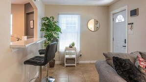 A modern living room with a grey sofa, a small side table, a potted plant, a round mirror, and a white door. - Quarry Downtown Airport 10 mins or less (San Antonio)