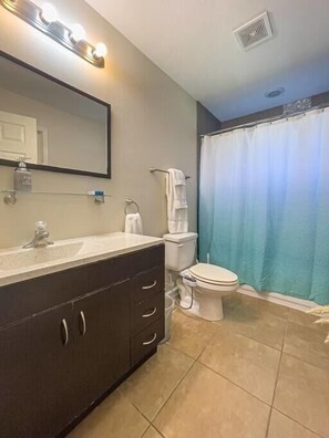 Un baño con tocador de madera oscura, inodoro blanco y cortina de ducha.