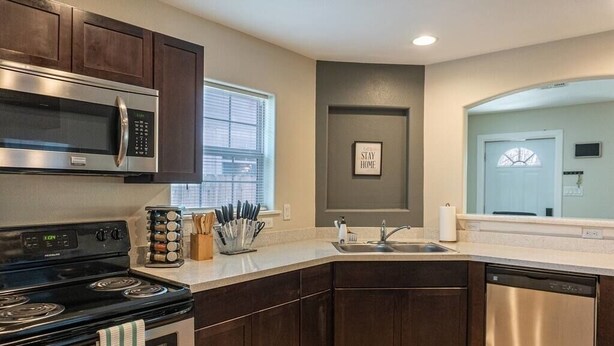 A modern kitchen with dark wood cabinets, stainless steel appliances, and a large window. - Quarry Downtown Airport 10 mins or less (San Antonio)