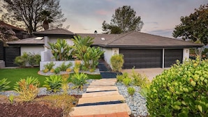 Une maison moderne dotée d’une allée pavée, d’un garage et d’un jardin bien entretenu où poussent différentes espèces de plantes.