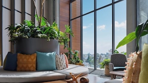 A modern living room with a large window, a sofa with cushions, a coffee table with a wooden sculpture, and a potted plant. - voco Guadalajara Neruda by IHG (Guadalajara)