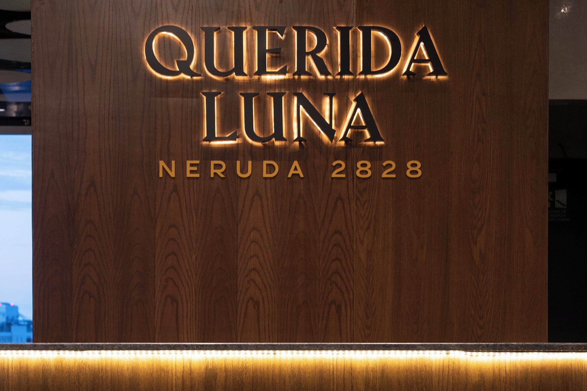 A wooden reception desk with illuminated lettering for 'QUERIDA LUNA' and the address 'NERUDA 2828'.