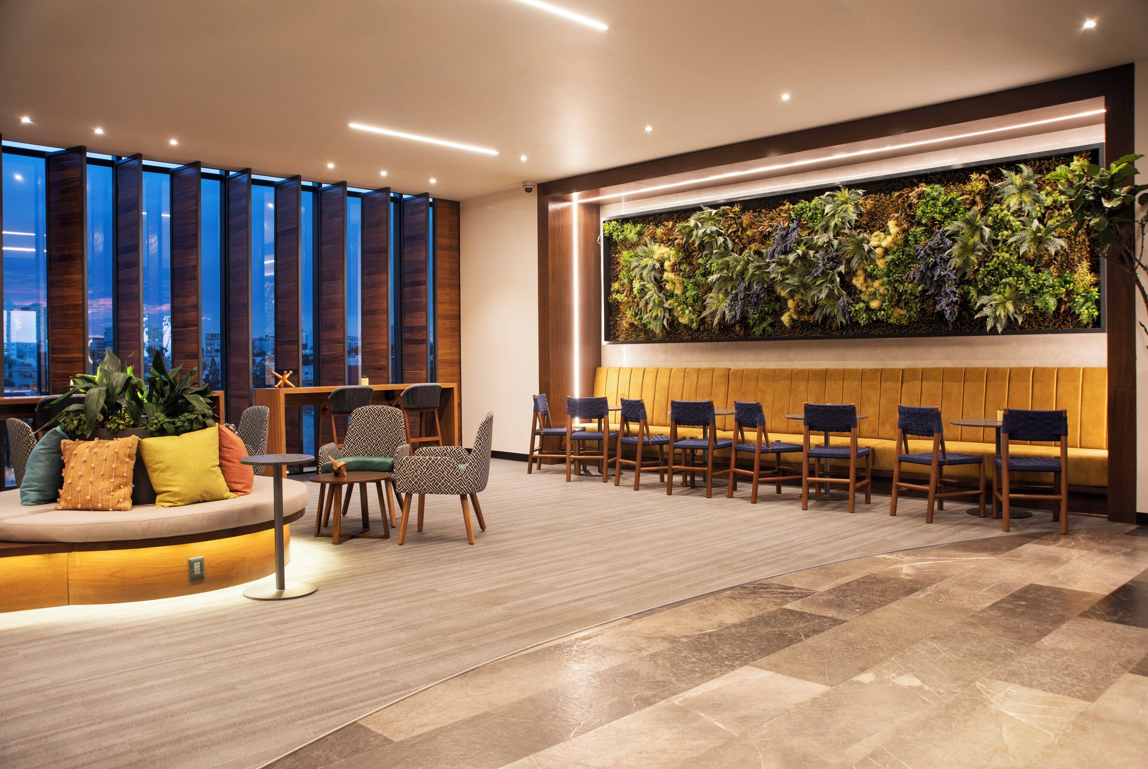 A modern hotel lobby with a seating area, a vertical garden wall, and a view of the cityscape through large windows.