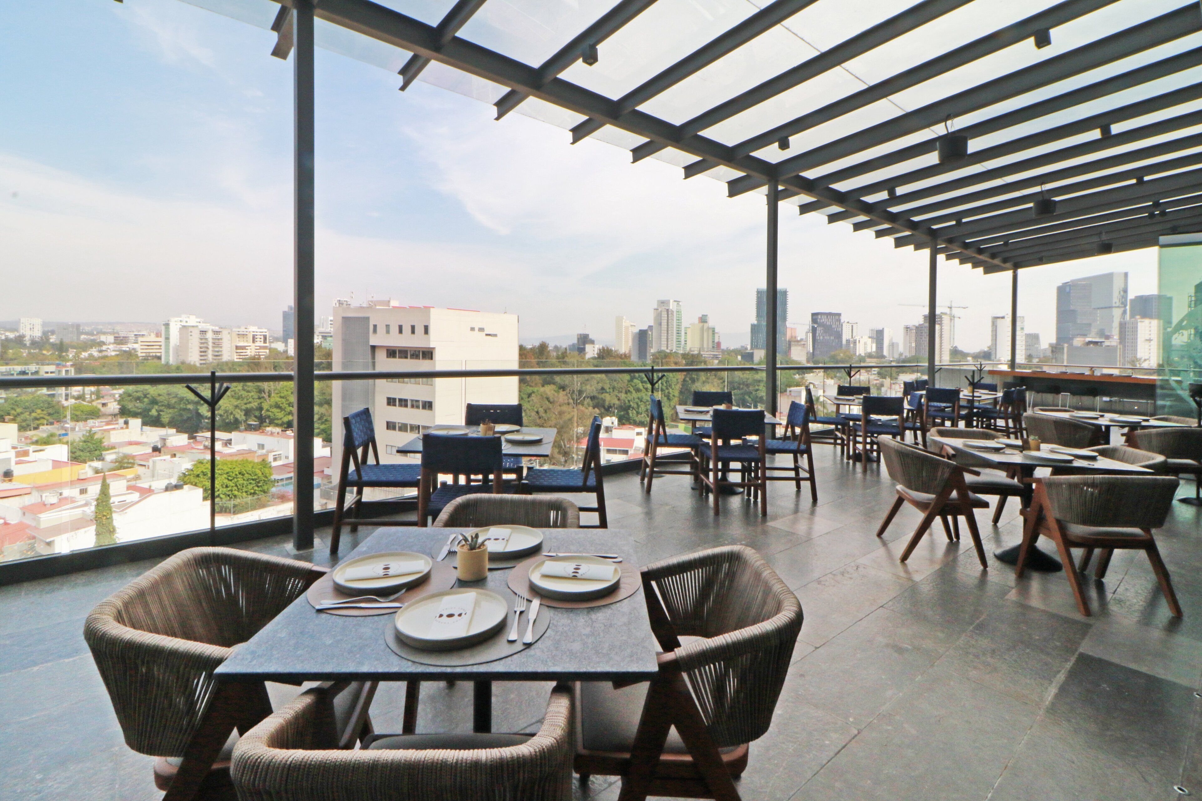 A rooftop restaurant with tables set for dining, overlooking a cityscape.