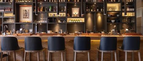 A bar area with multiple shelves of bottles and glasses, bar stools, and a counter with a bartender.