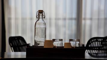A clear glass bottle on a table with two cups and a small box, set against a window with blinds.