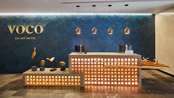 A reception area with a herringbone patterned wall, a reception desk with a modern design, and pendant lighting.