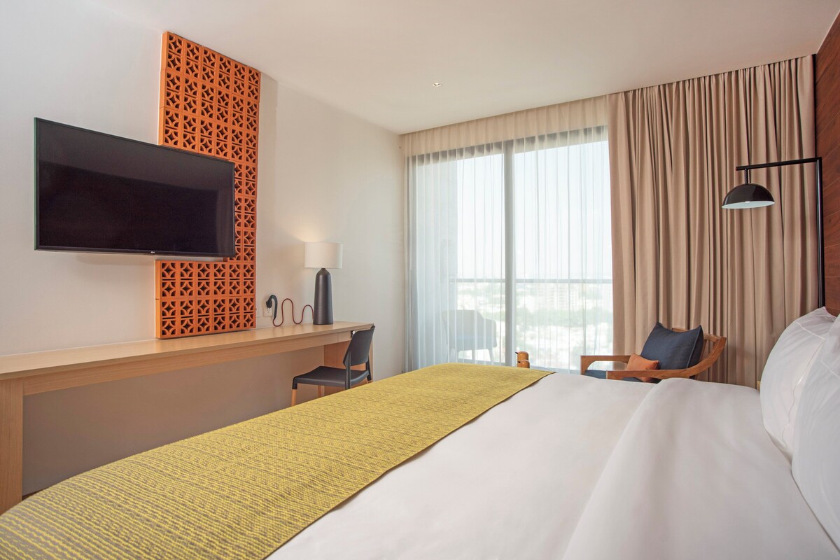 A hotel room with a bed, a desk, a television, and a window with curtains.
