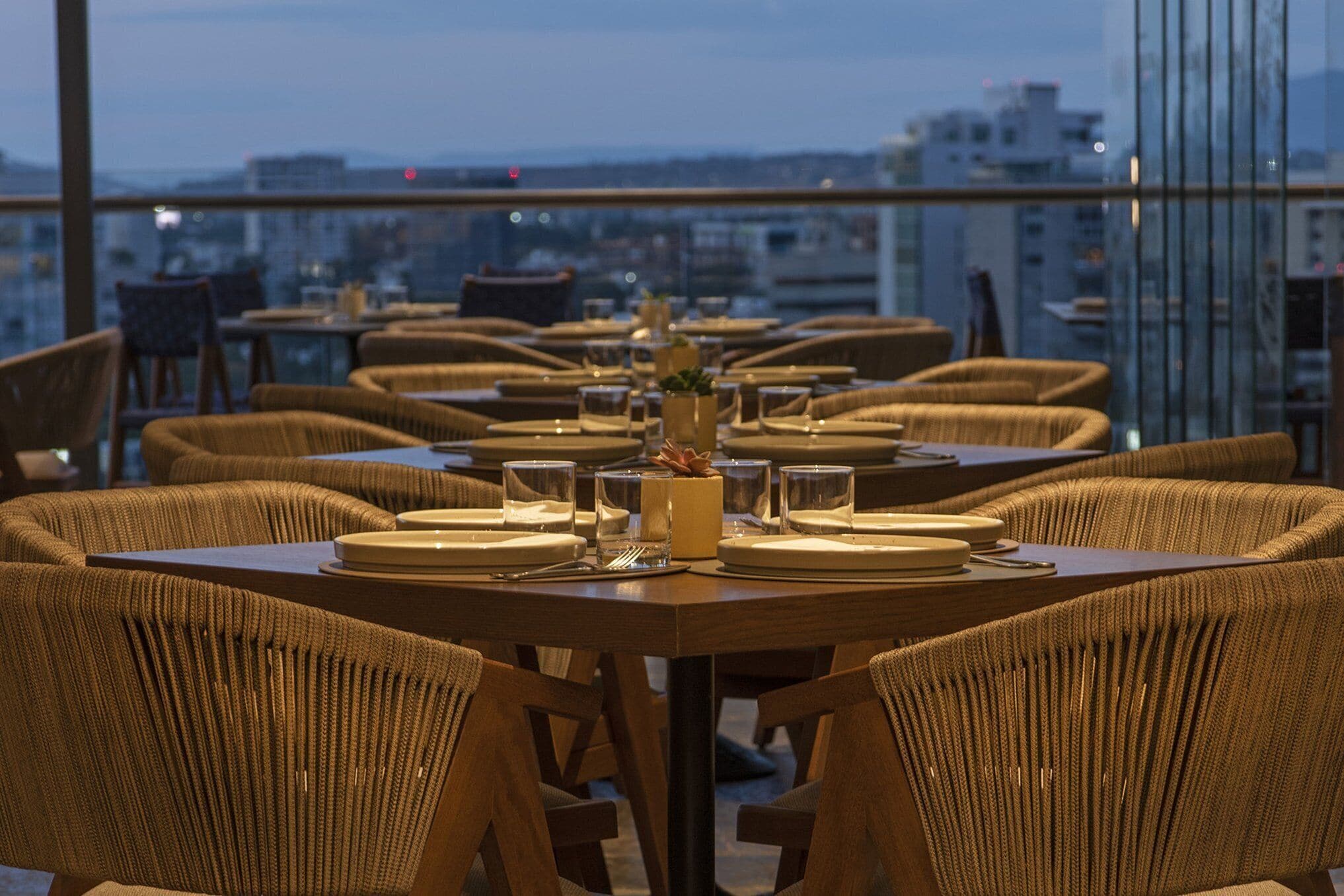 A restaurant with round tables and wicker chairs, set for dining with plates and glasses.
