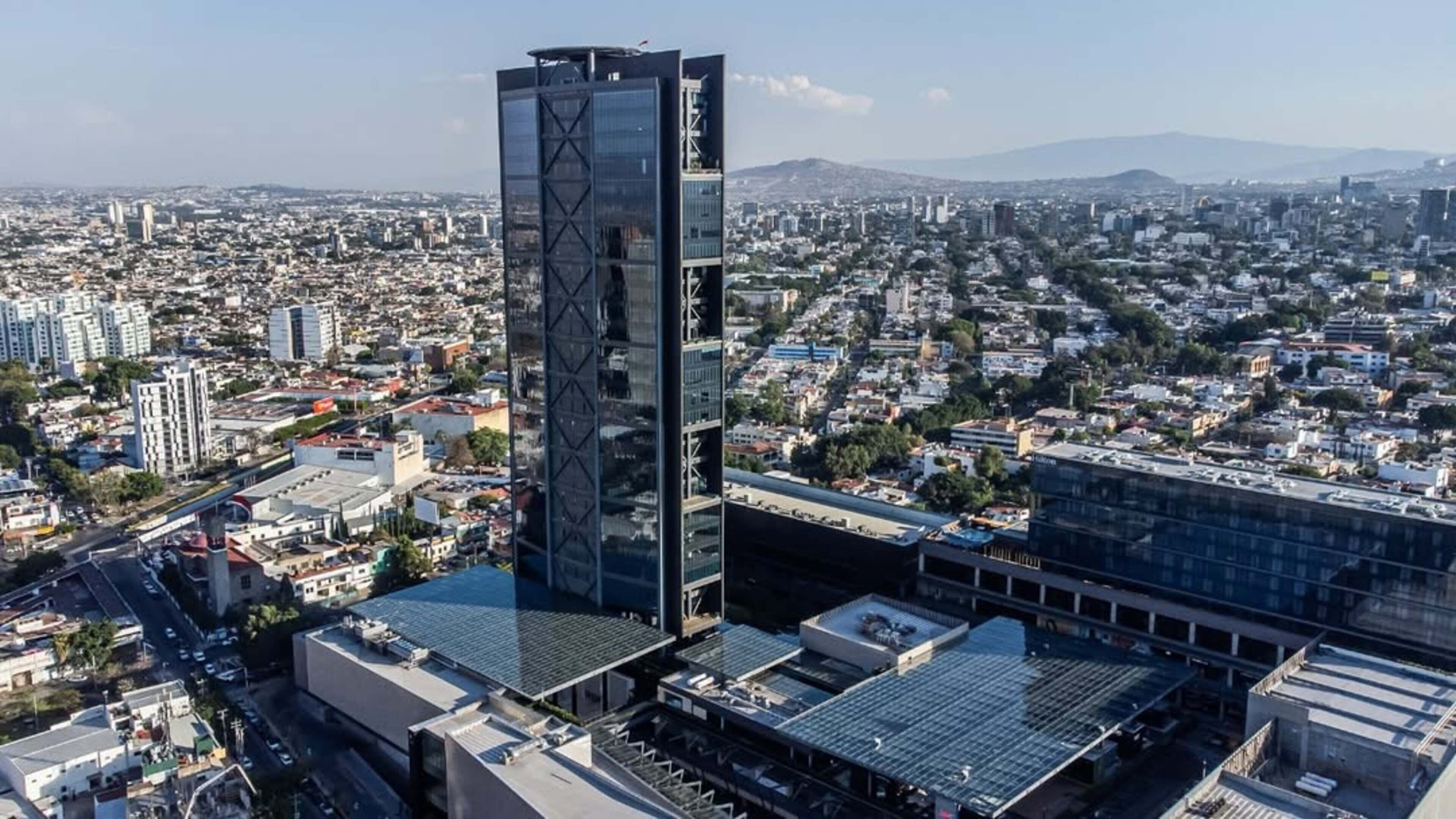Un edificio de gran altura con fachada de vidrio moderna, rodeado por una zona urbana densamente poblada con diversos edificios y calles.
