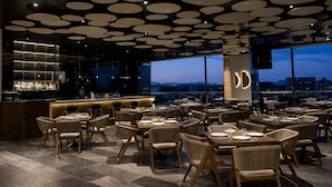 A restaurant with a modern interior, featuring a bar area, multiple dining tables, and chairs. - voco Guadalajara Neruda by IHG (Guadalajara)