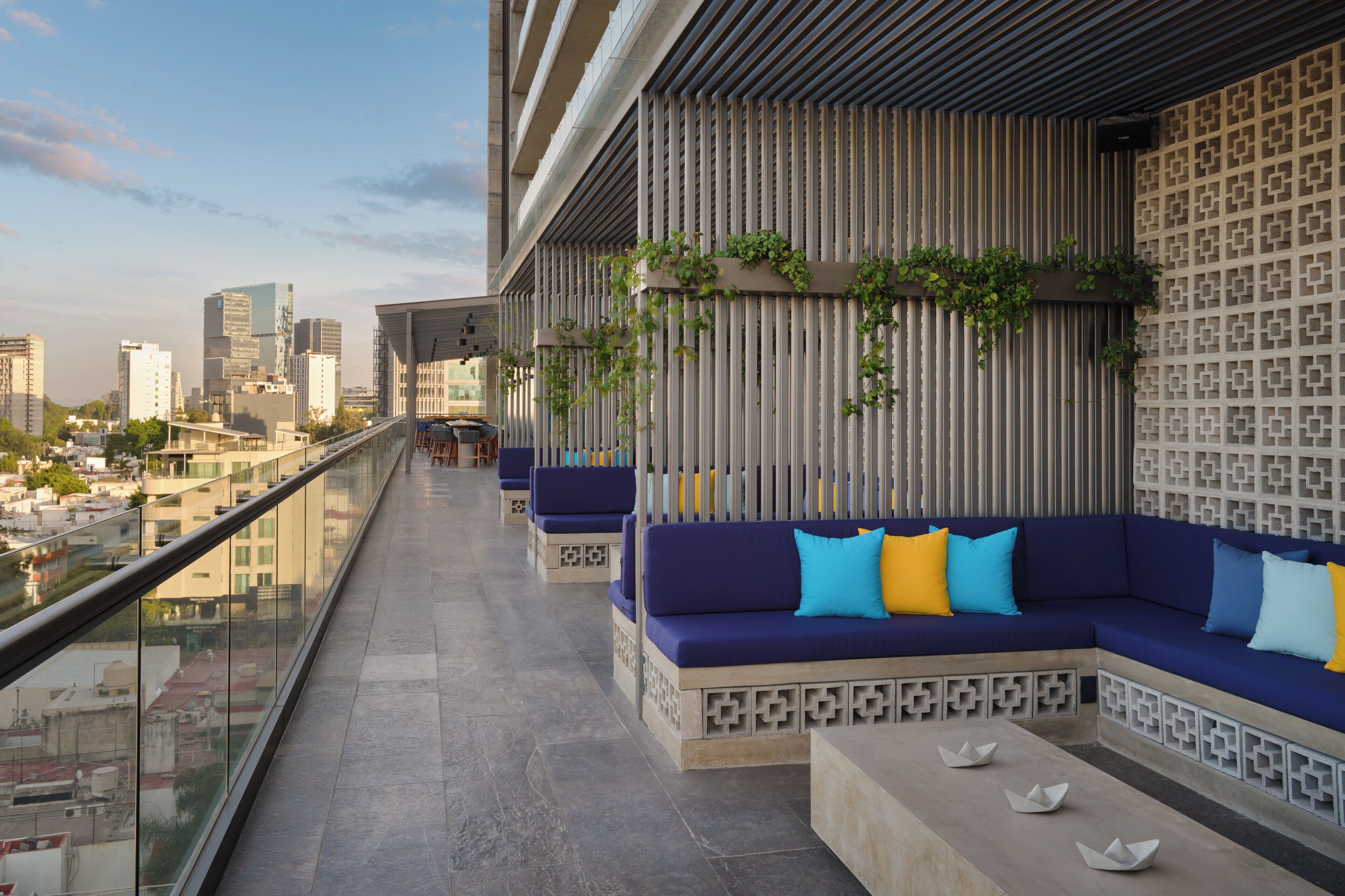 A rooftop terrace with a long seating area, a patterned wall, and a city view.