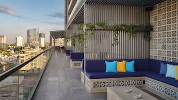 A rooftop terrace with a long seating area, a patterned wall, and a city view.